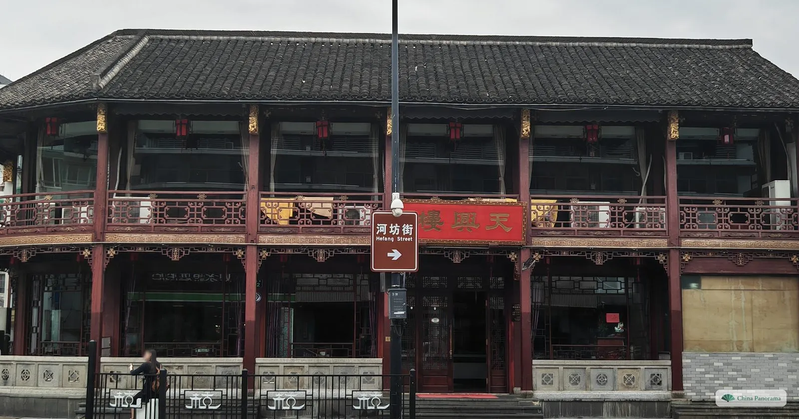 A long two-storey wooden building with red balconies and a brown street sign in front