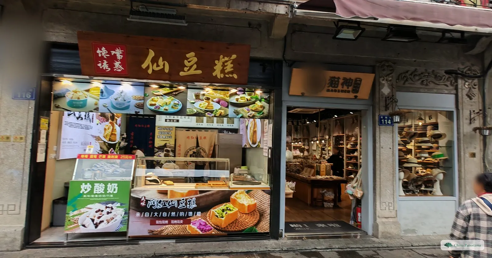 A snack shop window with a gold signboard of three characters and photos of desserts, a hat shop next door