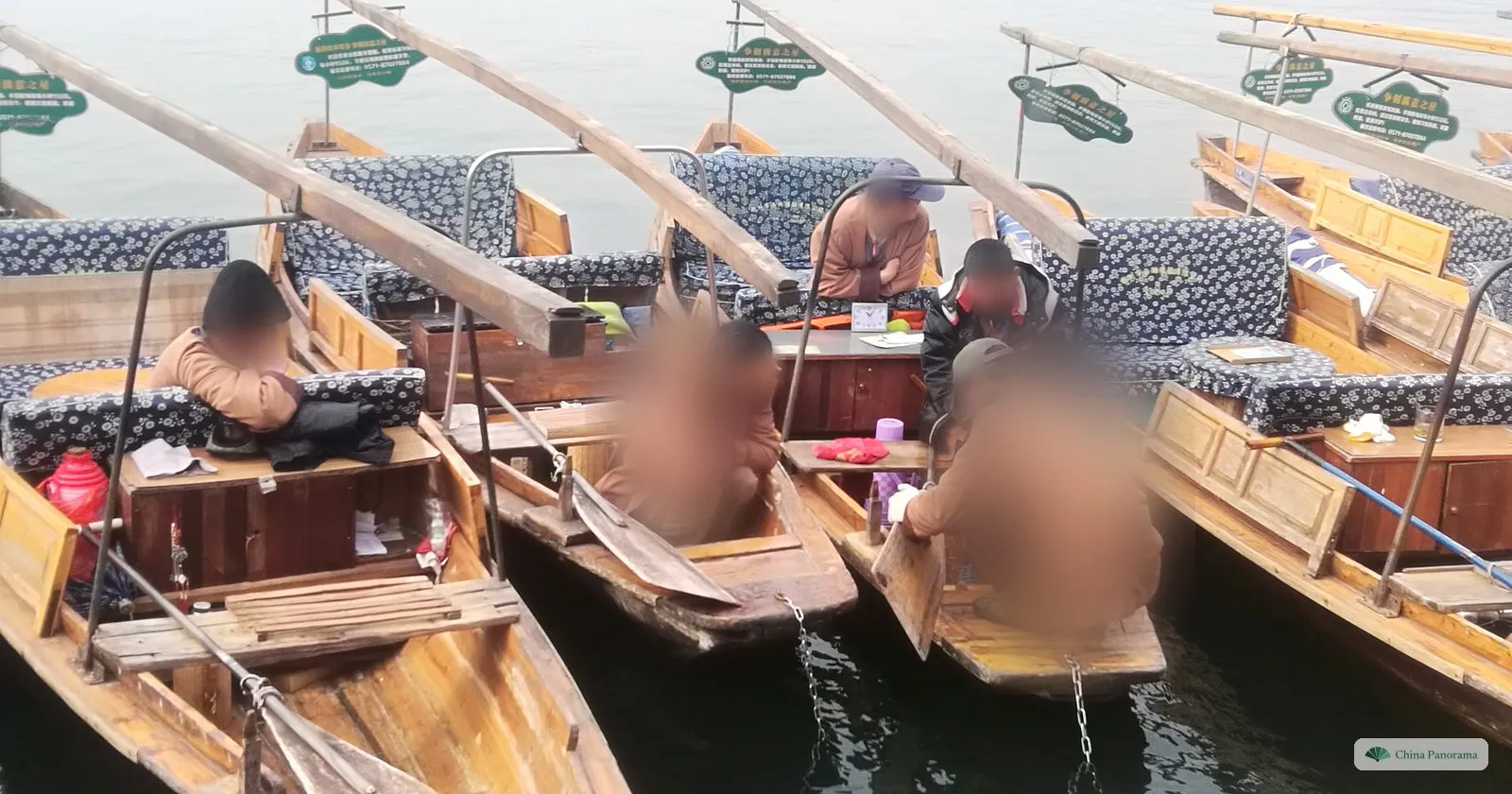 Boatmen in winter jackets sitting in wooden rowing boats with blue patterned cushions, waiting for passengers