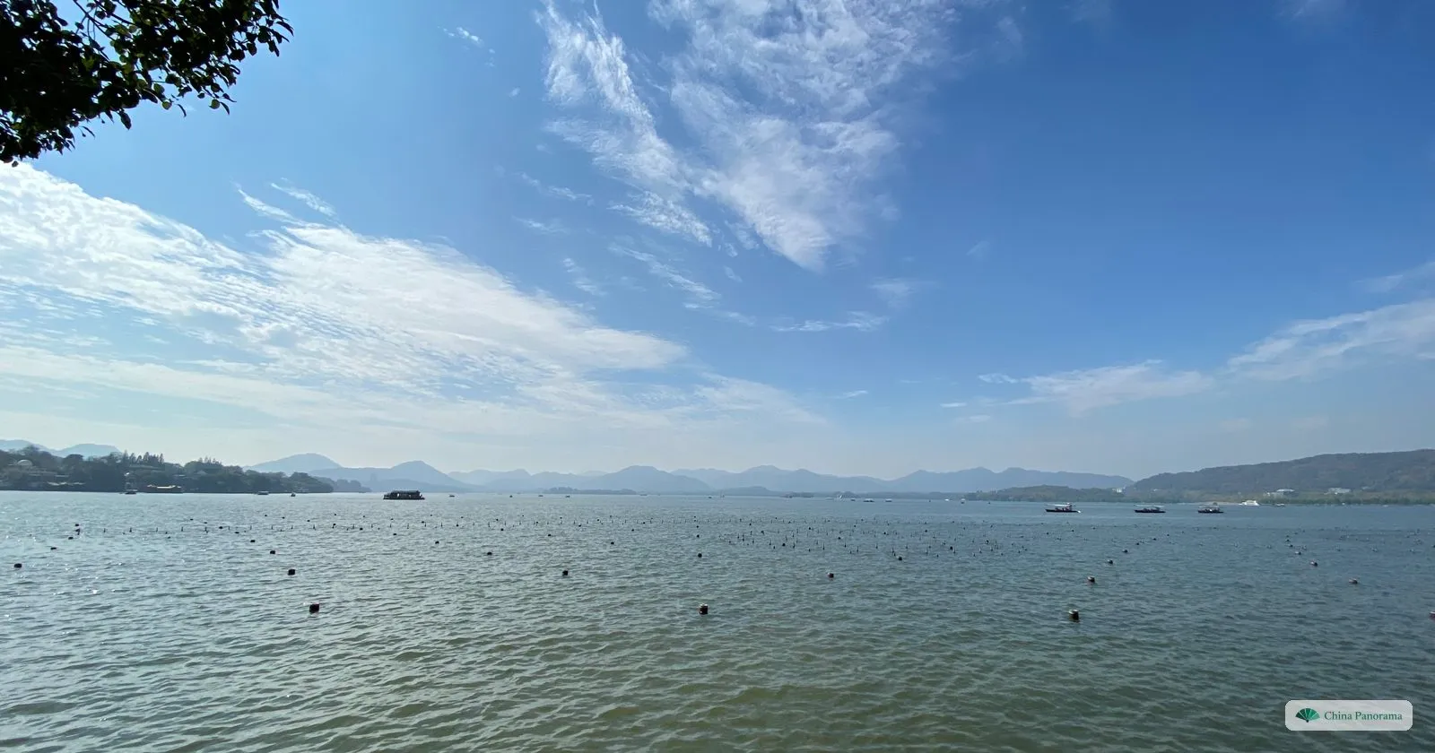 A wide calm lake under a blue sky with wispy clouds, low hills on the far shore