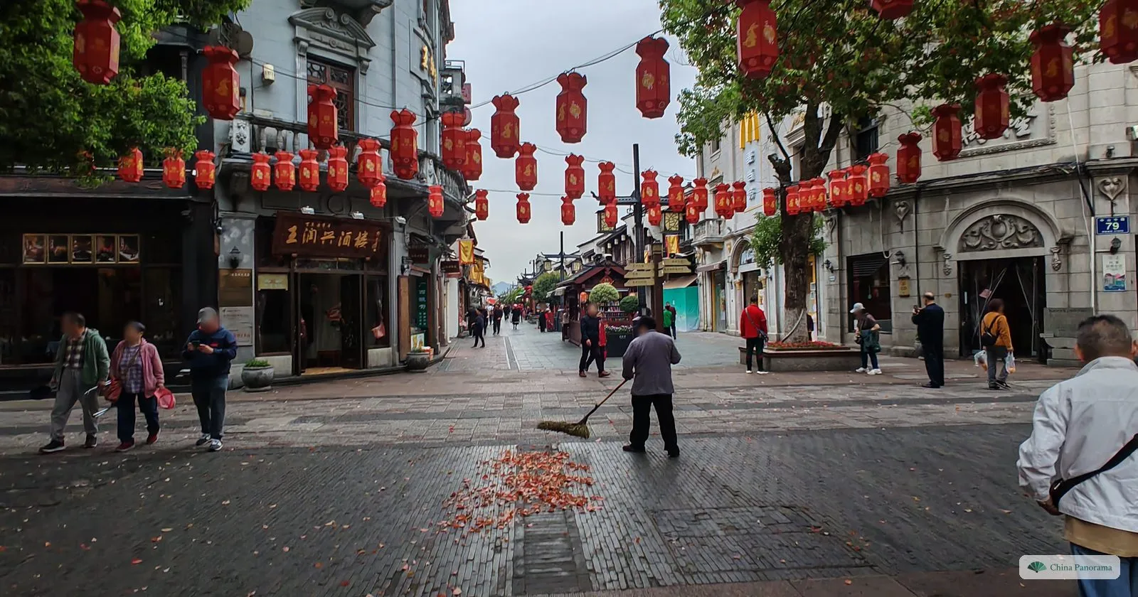 A wide paved pedestrian street under rows of red lanterns, a street sweeper at work and a few early walkers