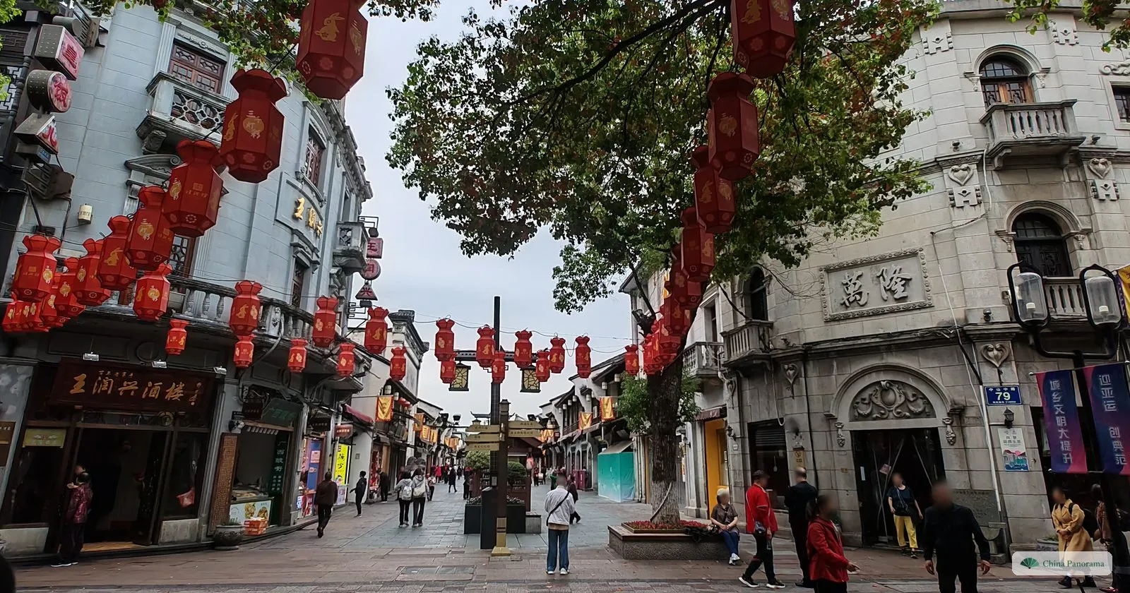 A pedestrian street with grey stone Republic-era buildings and rows of red lanterns hung between them