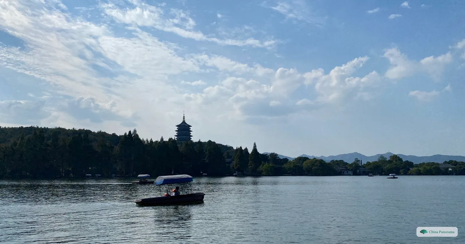 A tall pagoda on a wooded hill across a lake, a small electric boat in front