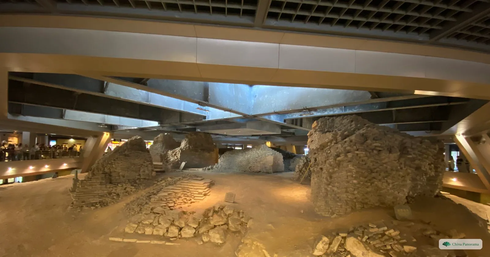 Ruined brick foundations of an old tower inside a modern hall, lit from above