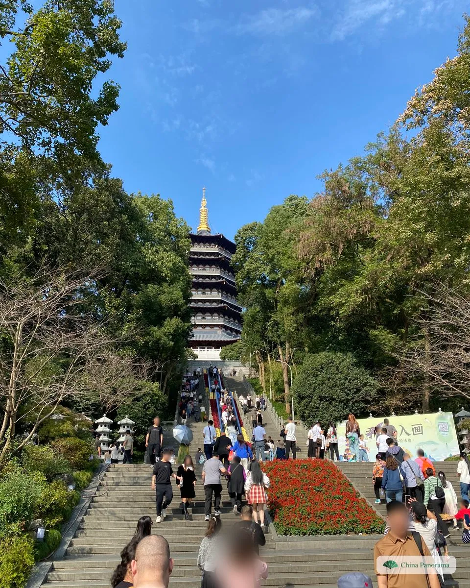 Broad stone steps crowded with visitors climbing towards a tall pagoda with many tiers and a golden spire