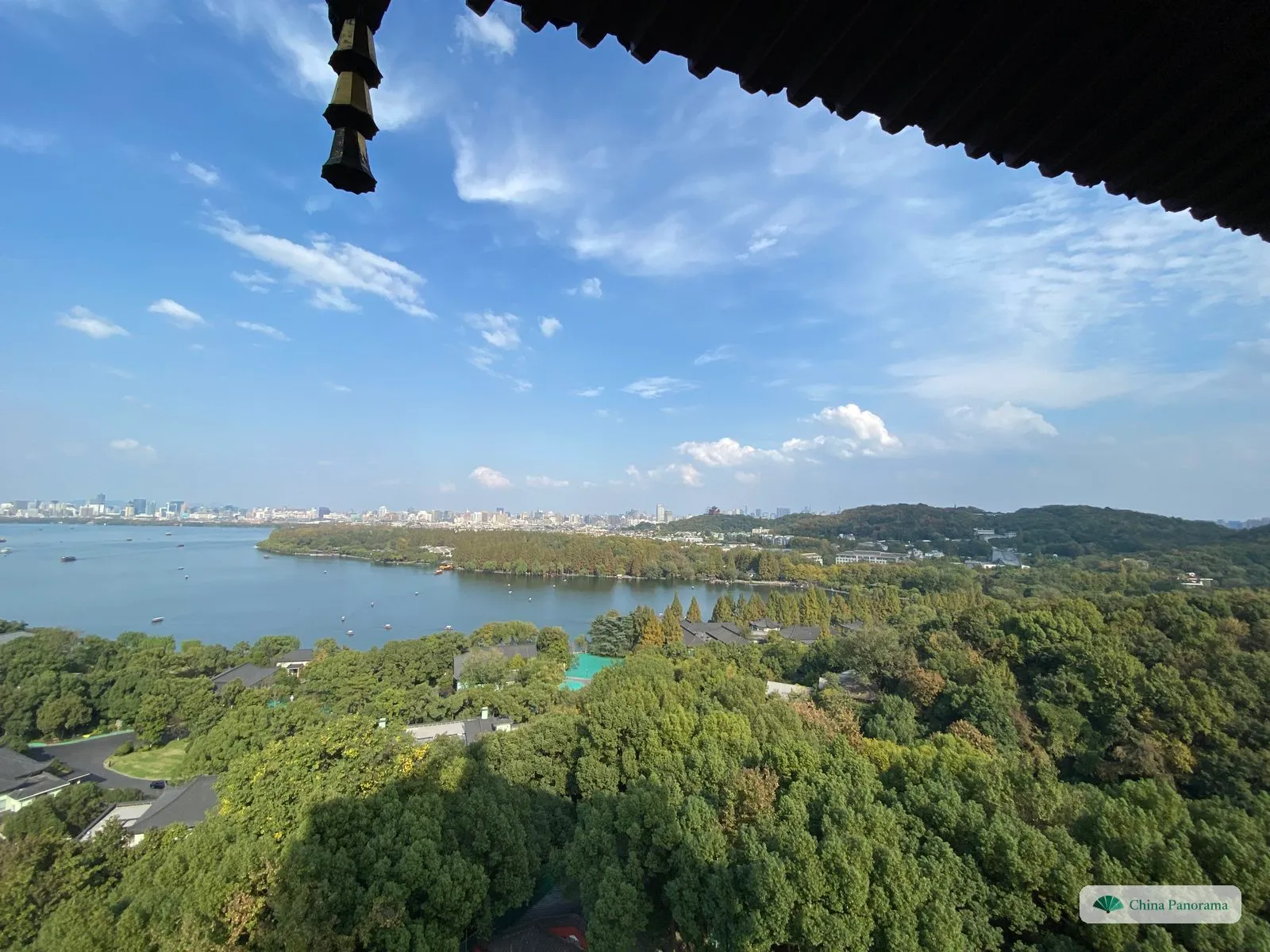 Looking down over trees to a lake and a wooded shore, the skyline of a city along the far side and a hill with a tower on the right