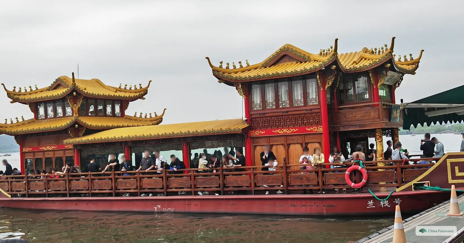 A large painted pleasure boat with golden upturned roofs and red railings at a pier, passengers on deck