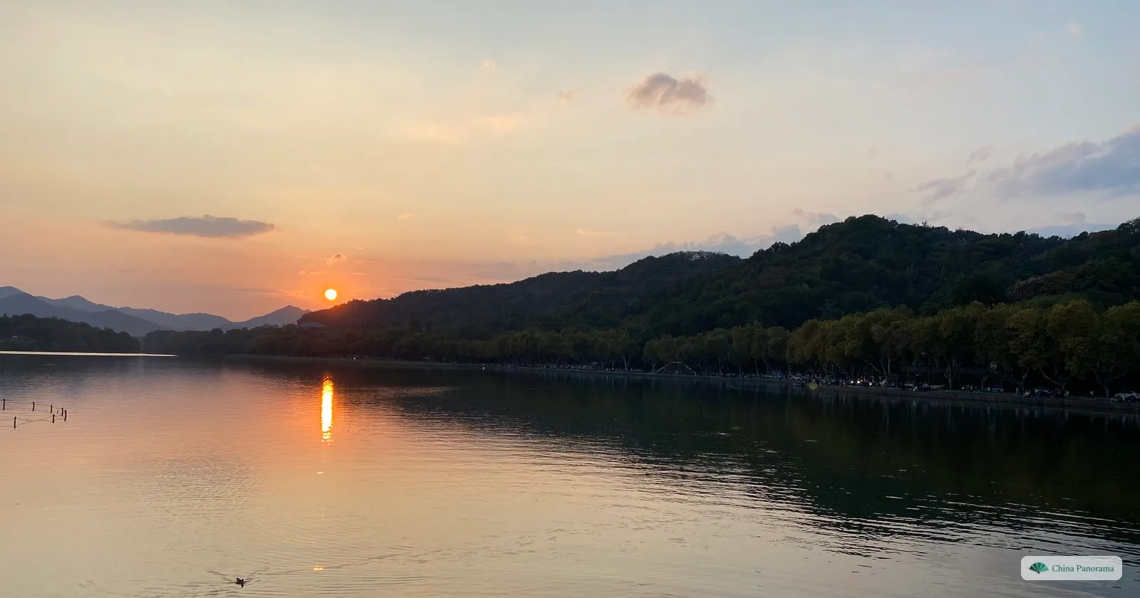 The setting sun over a calm lake, its reflection on the water and a long wooded ridge