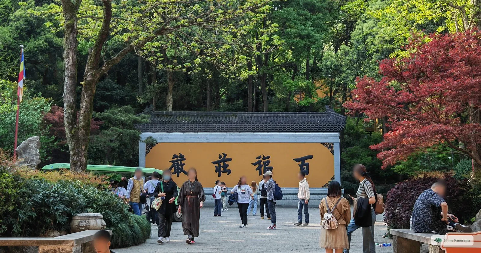 A long yellow screen wall with four large characters under a grey-tiled roof, red and green maples, visitors on the square
