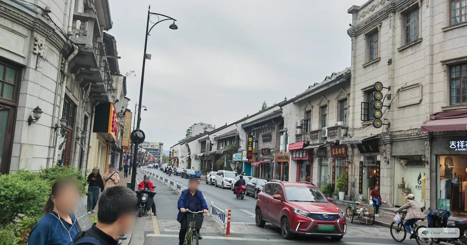 A street of grey stone facades with balconies and old shop signs, cars, cyclists and pedestrians