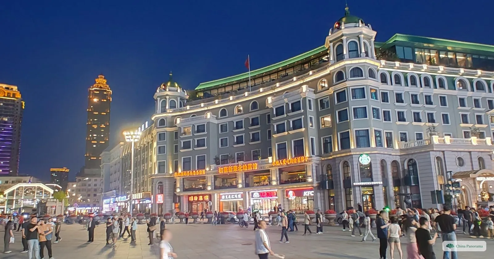 Central Street in Harbin at dusk, crowds in front of lit early-20th-century European facades