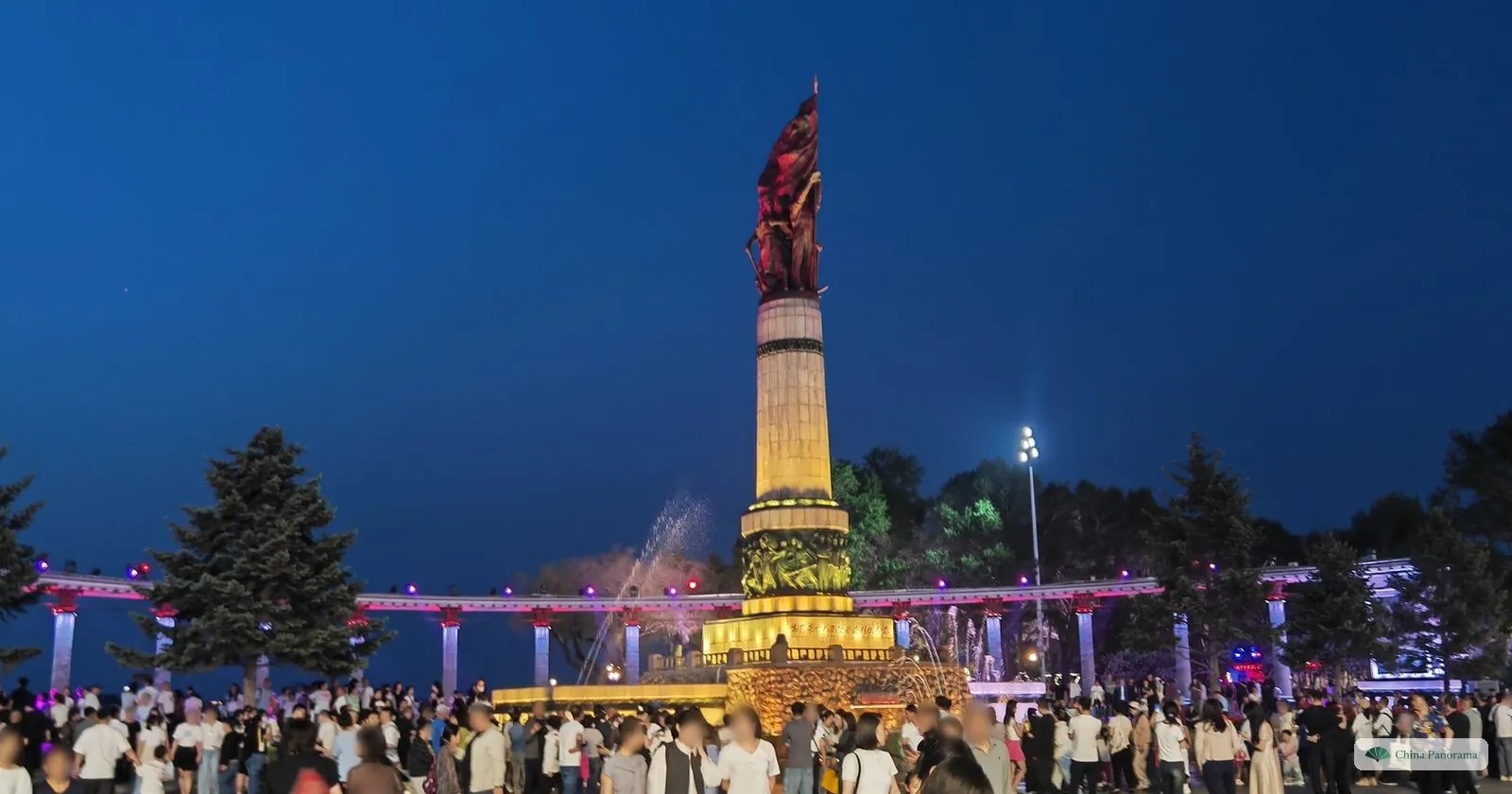 The 1958 Flood Control Monument in Harbin lit at blue hour, with crowds on the square