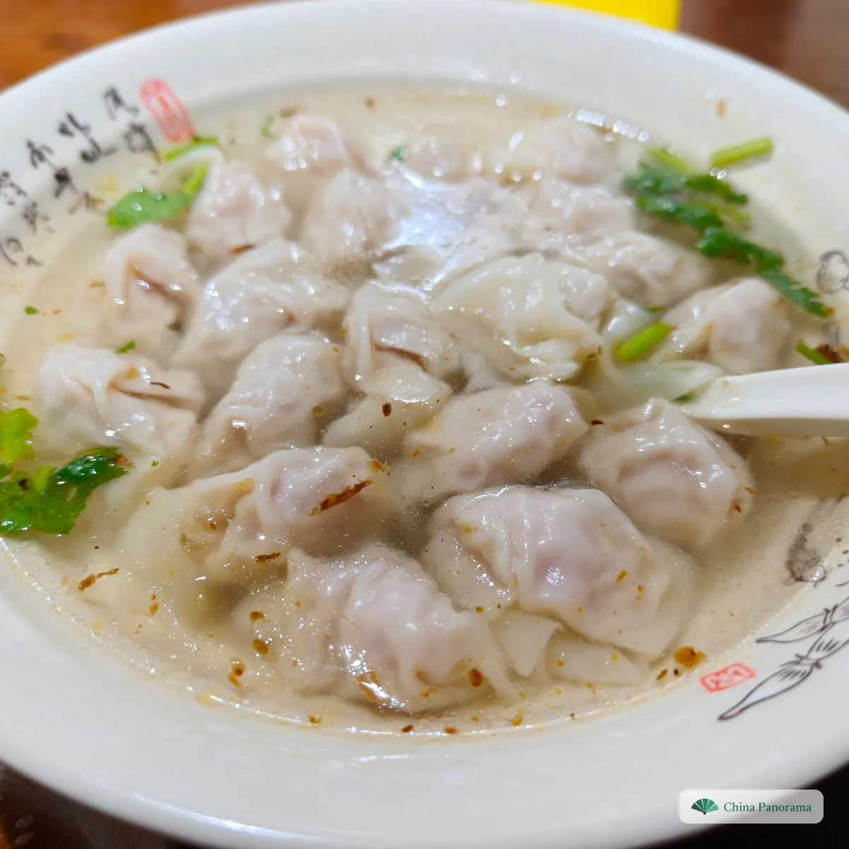 A pile of many tiny wontons in cloudy broth with dried shrimp, coriander and red flecks of chilli oil
