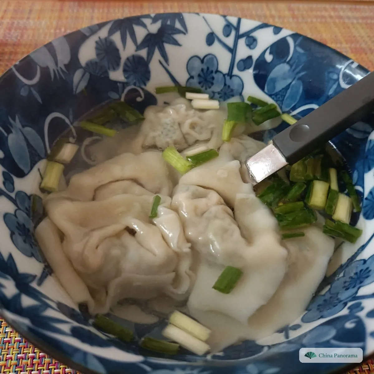 Big, loosely folded wontons in a little broth with spring onion, in a blue-and-white bowl with a metal spoon