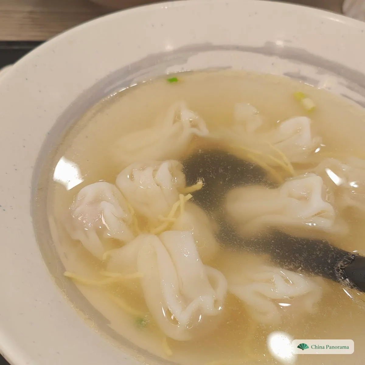 Loose, crumpled little wontons in clear broth with a sheet of dark seaweed and a few strands of egg, a black spoon at the side
