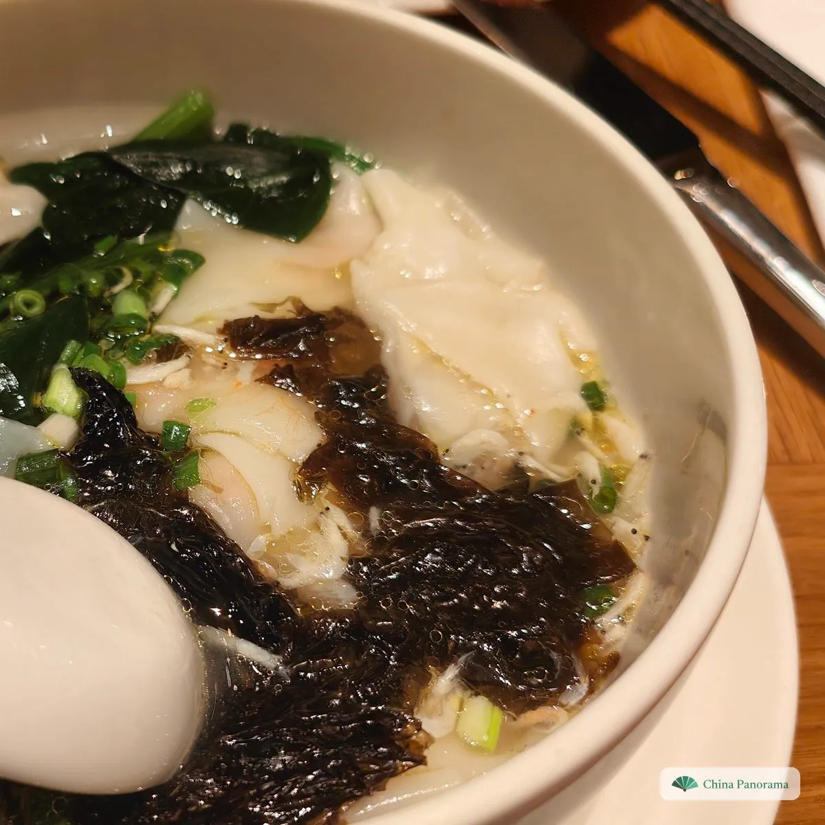 Smooth white wontons with dark green spinach and a heap of black seaweed in a deep white bowl