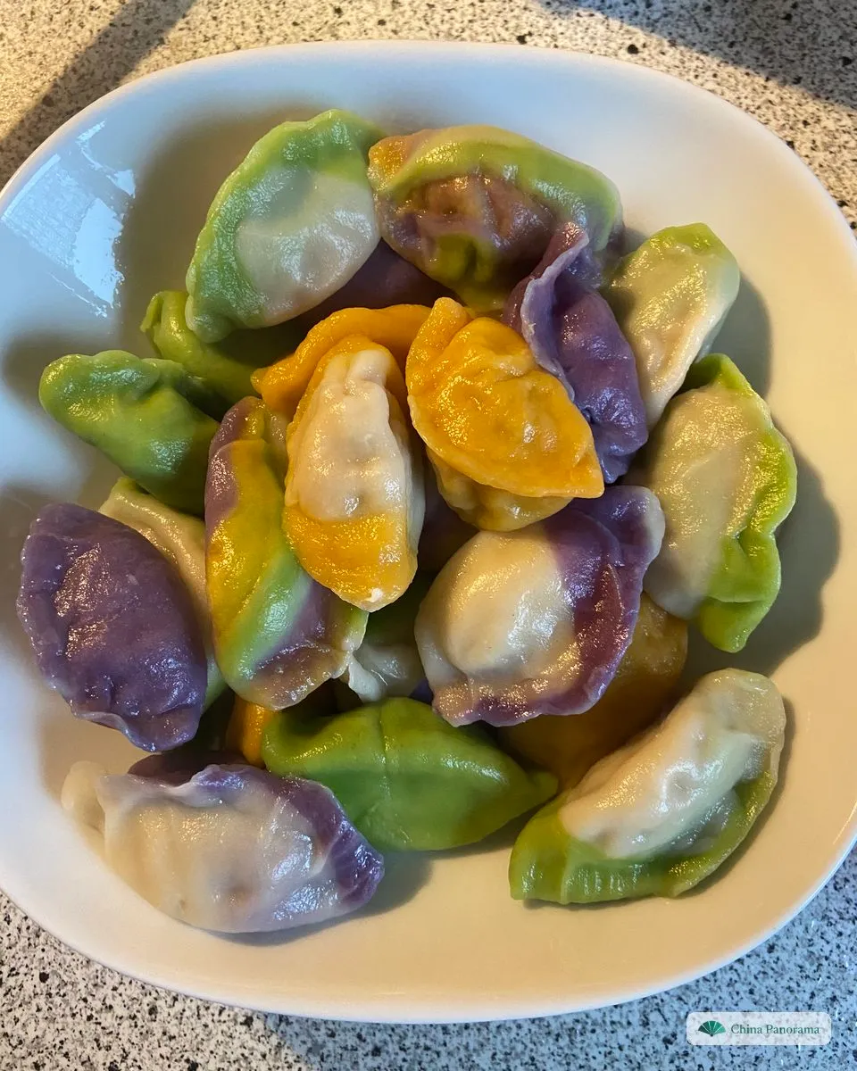A white bowl of boiled dumplings in green, yellow and purple, some in one colour, some white with a coloured edge, some striped in three colours