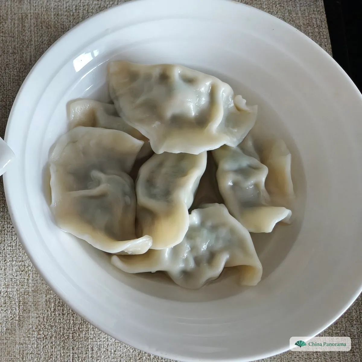 Pale, half-moon dumplings with green showing through the wrapper, piled in a white bowl without broth
