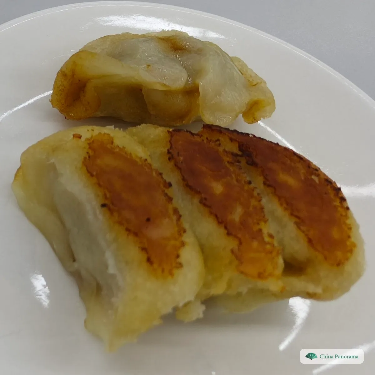 Pan-fried dumplings on a white plate, with dark golden fried strips along their sides
