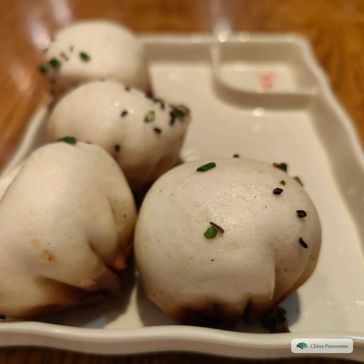 Round white buns with black sesame and chopped scallion on top and browned bottoms, on a white tray