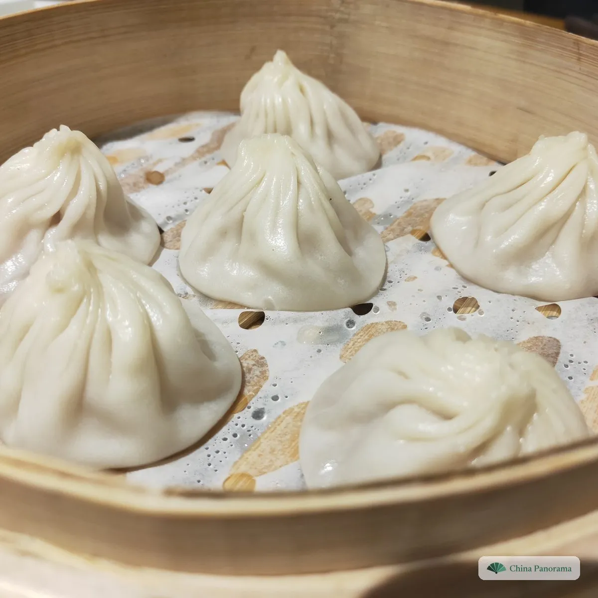 Six small round parcels with finely pleated tops gathered into a twist, in a bamboo steamer basket