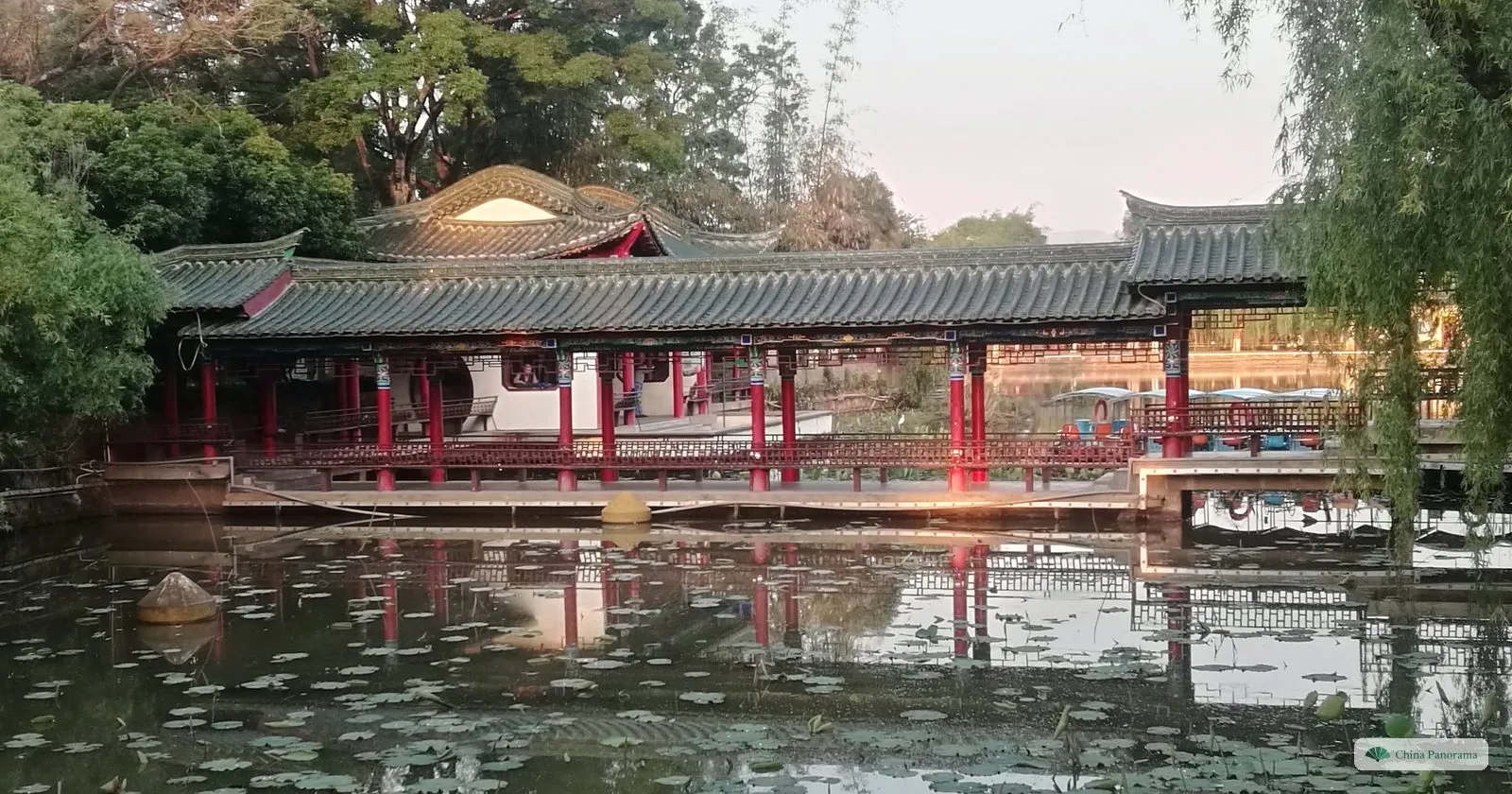 A long covered corridor with red columns and green roof tiles along a pond with water lilies