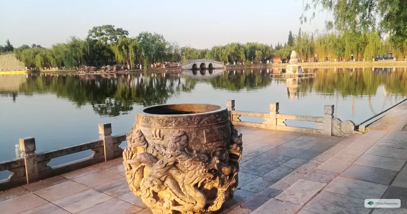 A large bronze urn covered in relief dragons on a stone terrace by the water