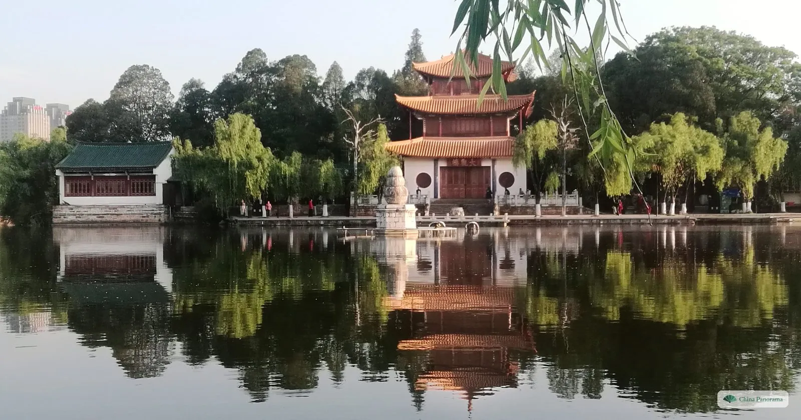 Daguan Tower, a three-storey pavilion with orange roofs, mirrored in a still pond among willows in early morning light