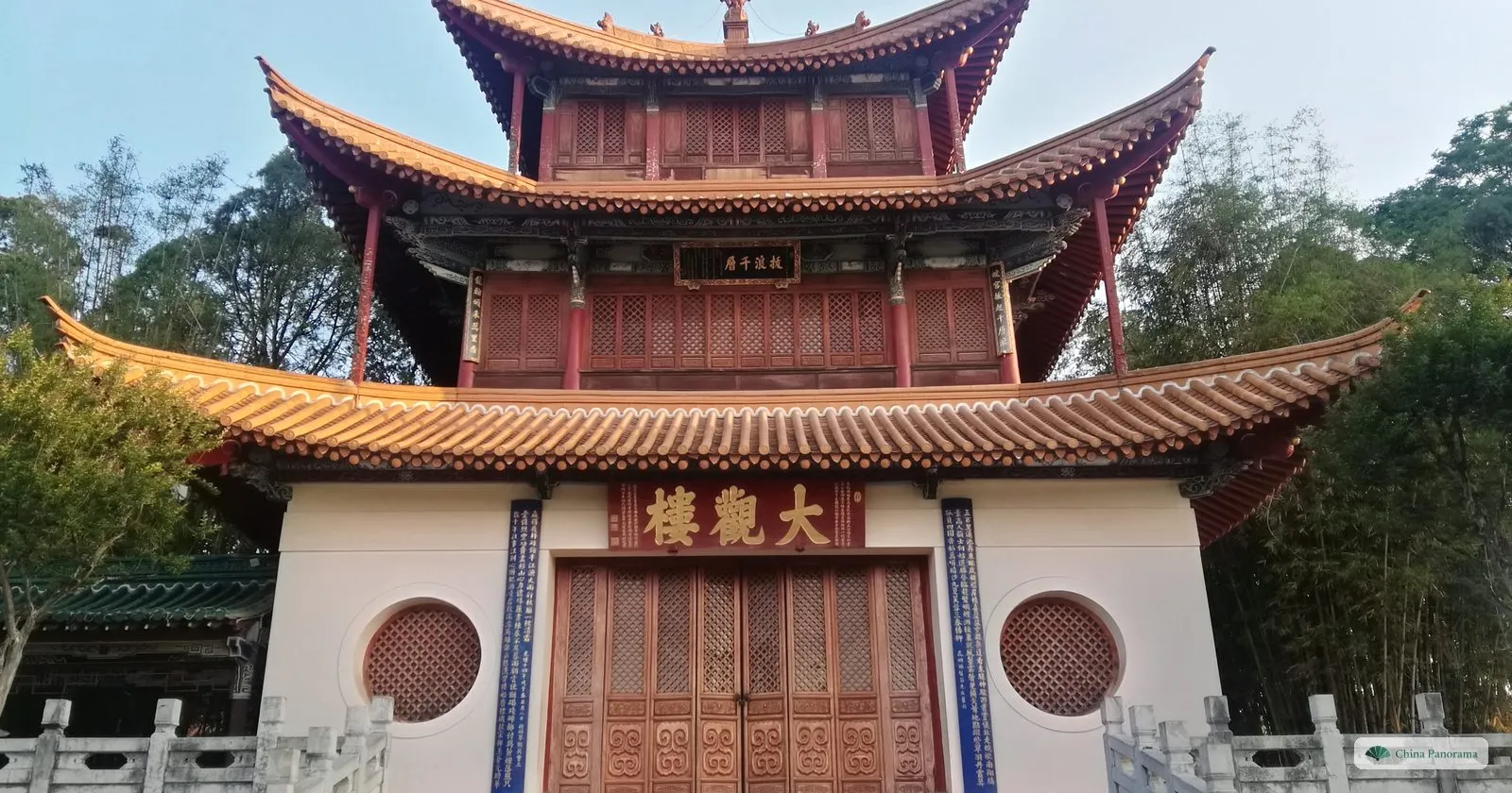 The front of a three-storey pavilion with curved orange roofs, a red plaque of three gold characters over carved wooden doors and two long blue boards of gold characters either side
