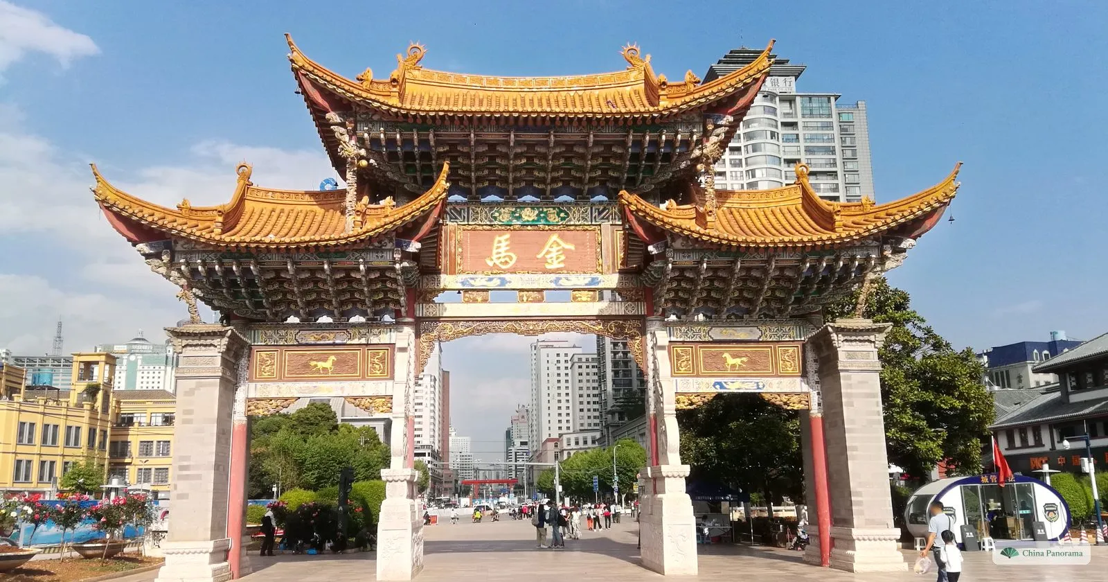 The painted Jinma arch with golden-yellow roofs and a red plaque, high-rise buildings beyond