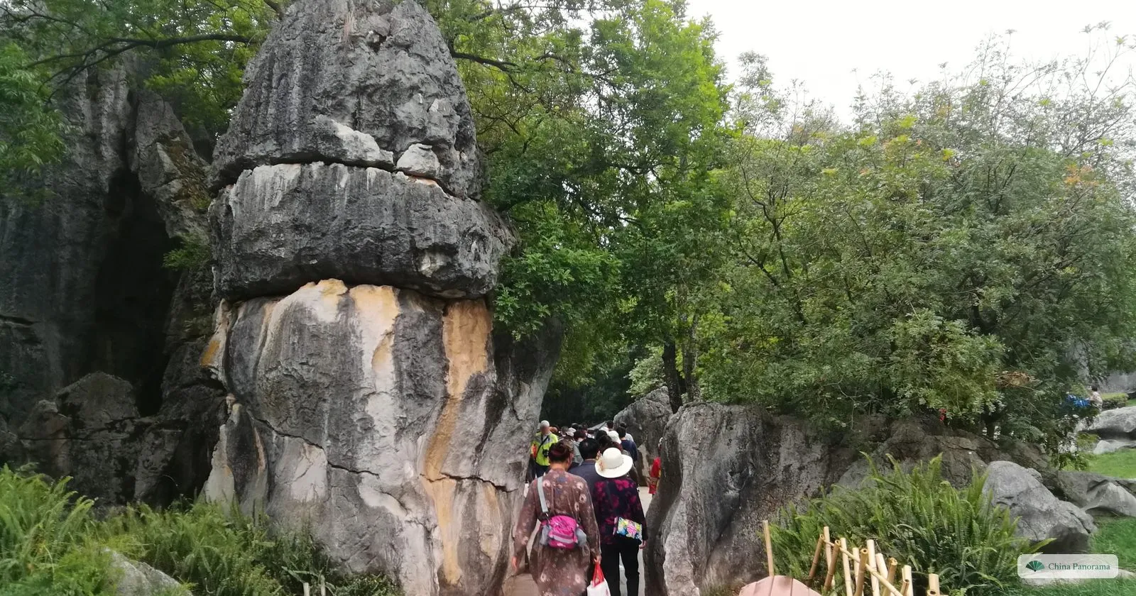 A great rock shaped like a mushroom, a weathered block balanced on a column, tourists walking past at its foot