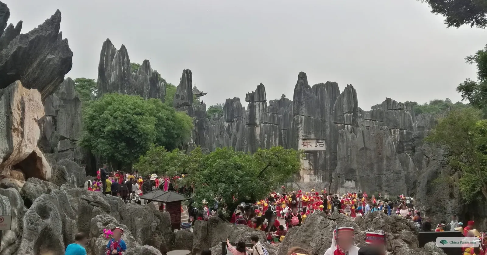 A crowd in red costumes and tourists in a hollow surrounded by grey limestone pinnacles