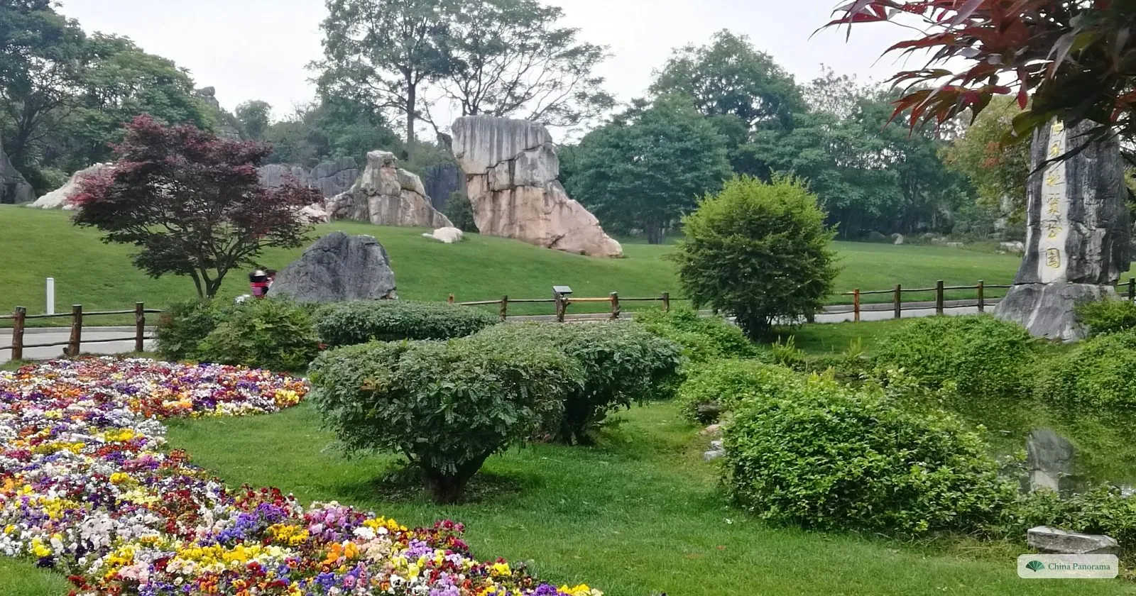 A sloping lawn with bands of pansies and shrubs, pale rock pillars scattered across it