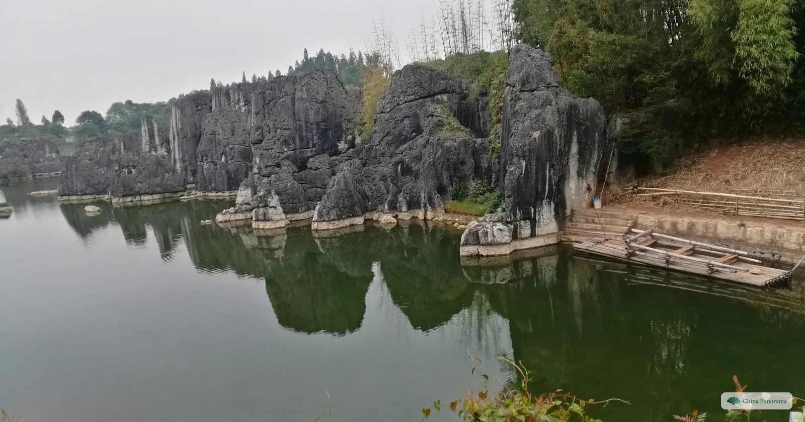 Grey rock pinnacles rising straight from a still green lake, with their reflections