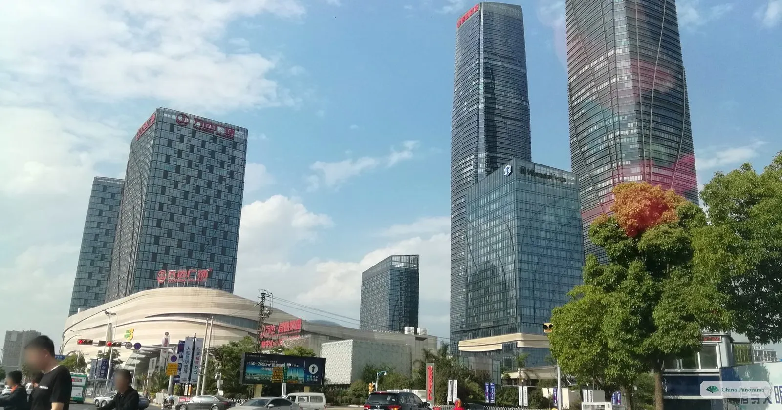 Two very tall glass skyscrapers next to a white shopping mall and an office block, a busy road junction in front