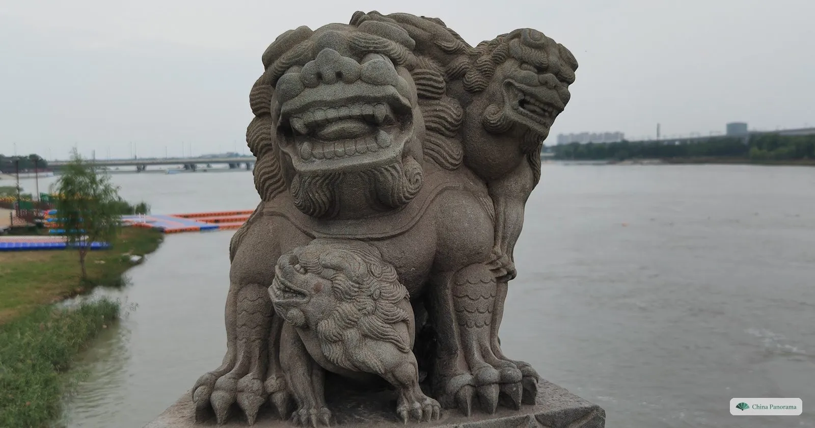 A stone lion on Lugou Bridge with one cub under its paw and another on its back, seen from the front