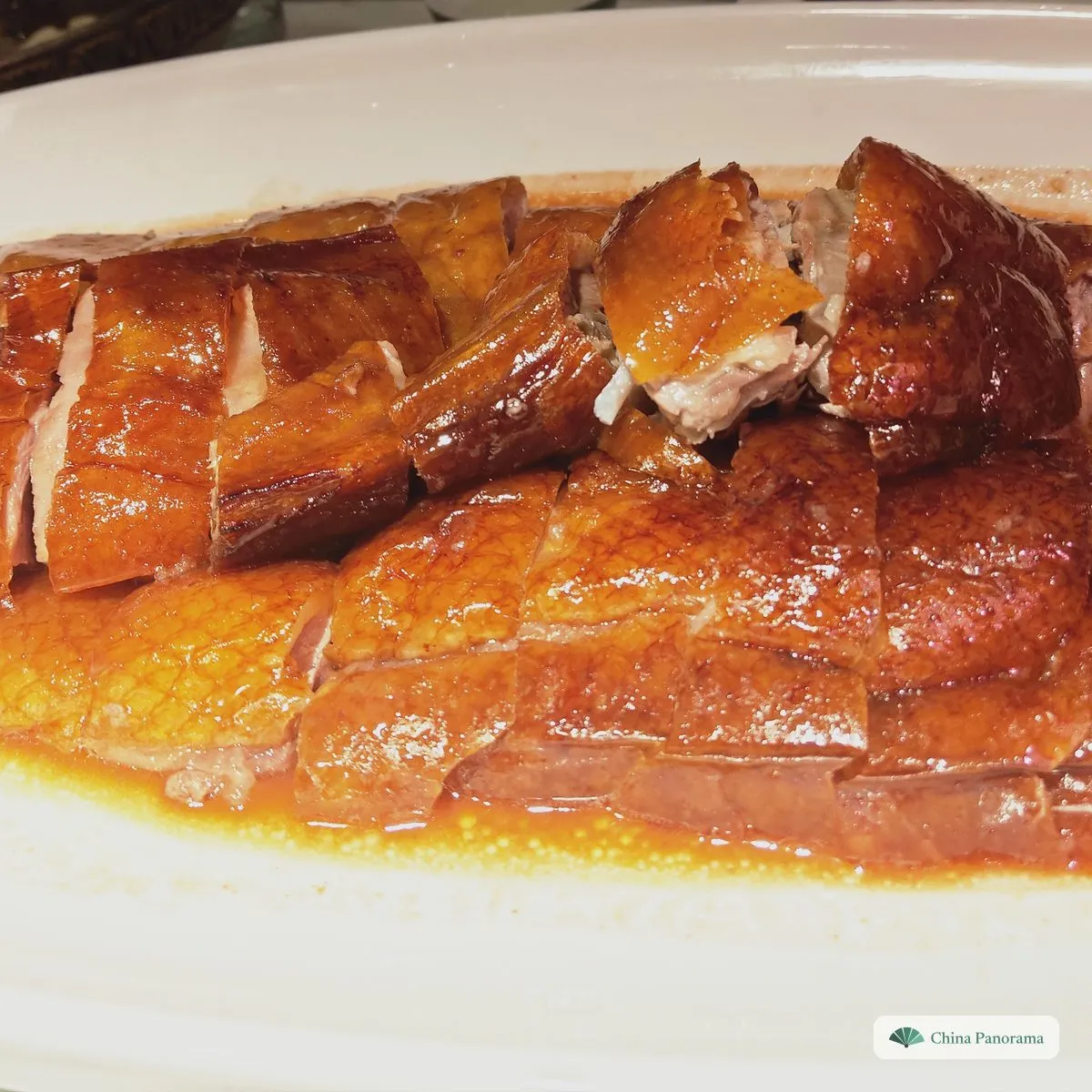 A whole roast goose chopped into pieces on an oval plate, with shiny golden-brown skin and a pool of orange juices