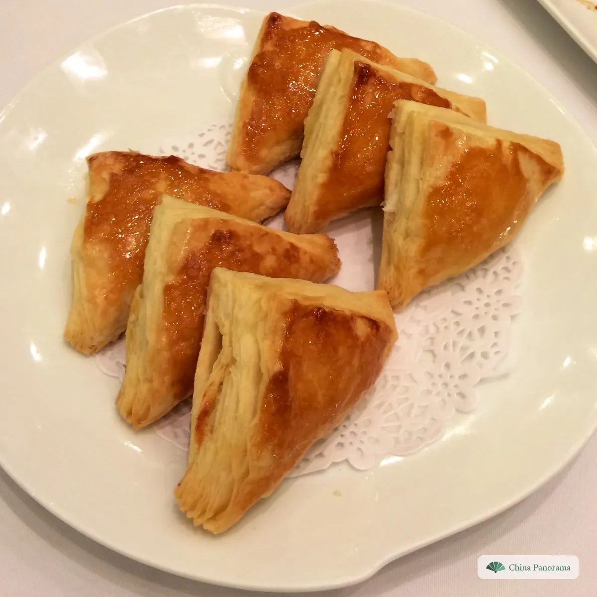 Five golden triangular puff pastries on a paper doily on a white plate
