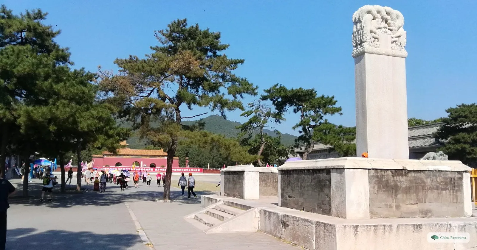 A tall white stone stele without an inscription on a stone platform on the plaza in front of Dingling, with pines and hills behind