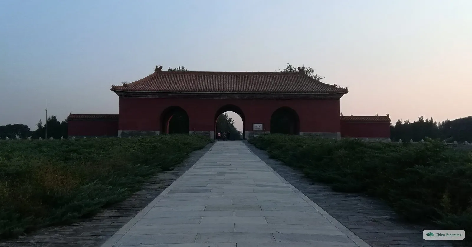 The Great Red Gate of the Ming Tombs at dawn: a red gatehouse with three arches at the end of a long stone path