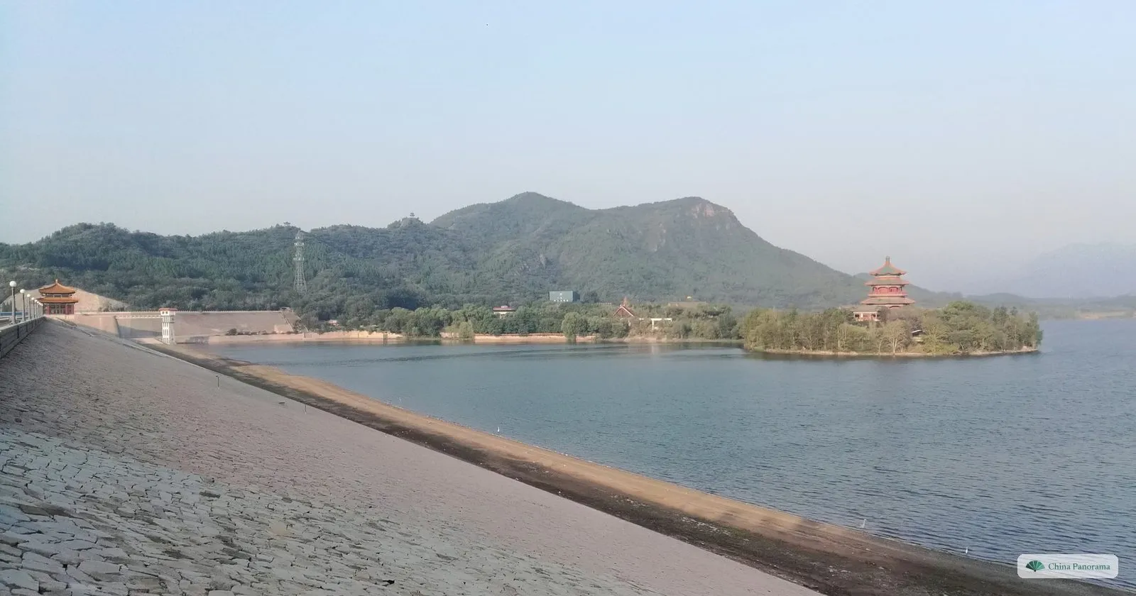 The Ming Tombs Reservoir in the early morning, with a pagoda on a wooded island and hills behind, seen from the stone-faced dam