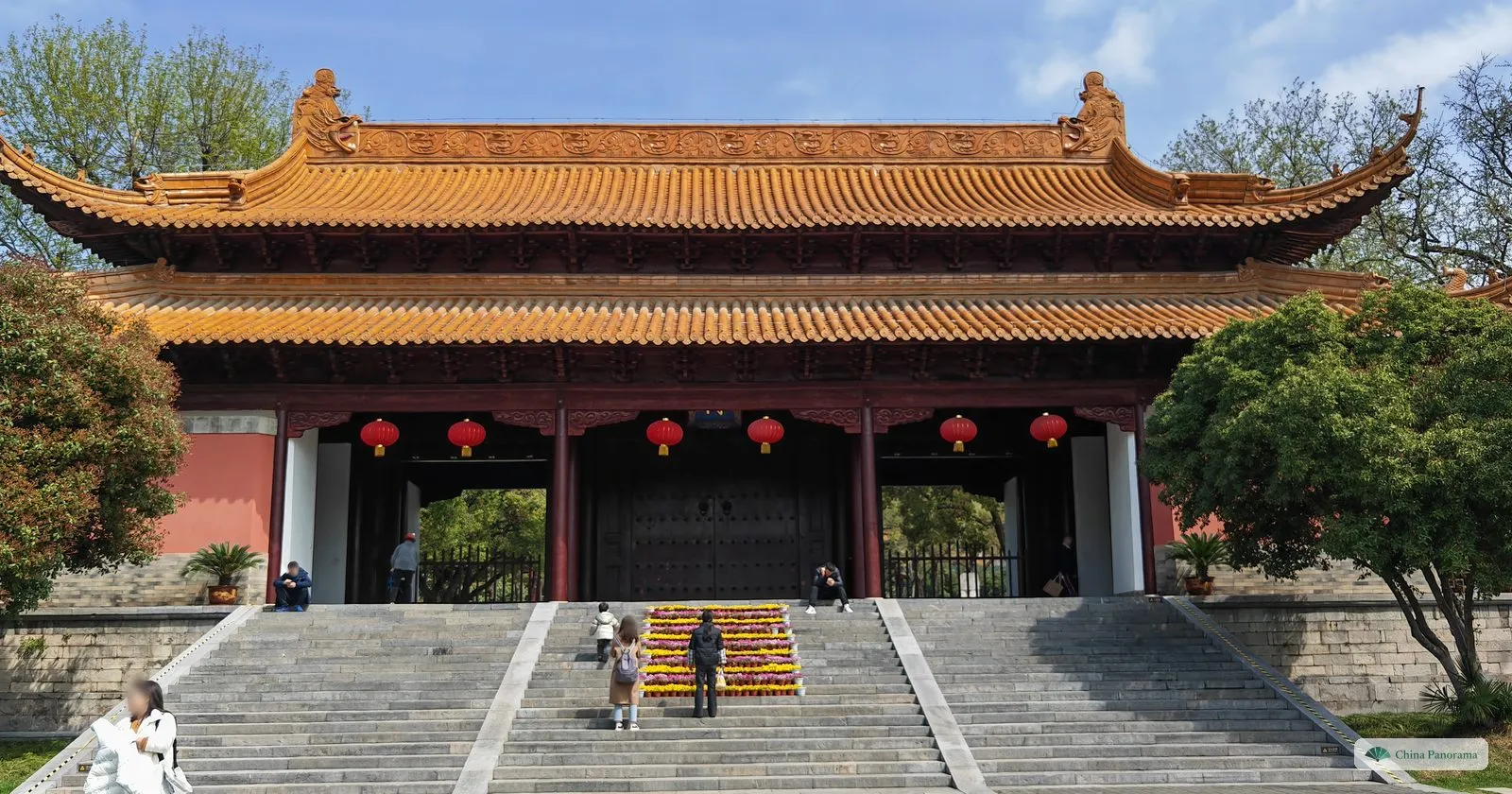 A wide gate hall with a double yellow tiled roof, red pillars and lanterns, at the top of three flights of stone steps