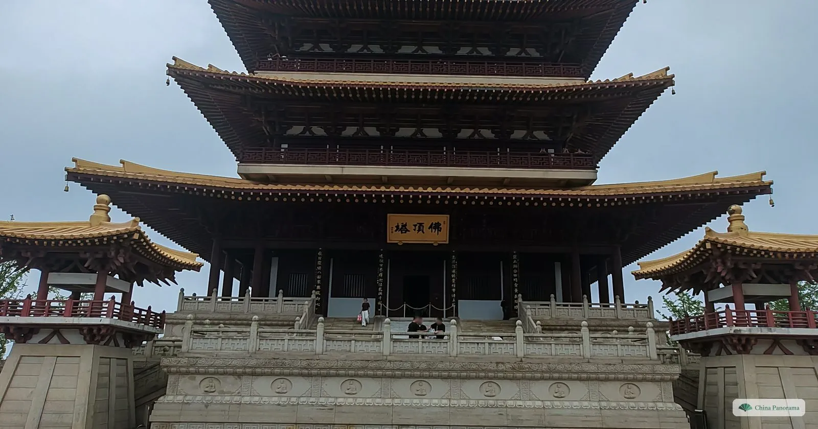 The base of a tall wooden-style pagoda with dark roofs on a white stone terrace, a black plaque 佛頂塔 over the door and two corner pavilions