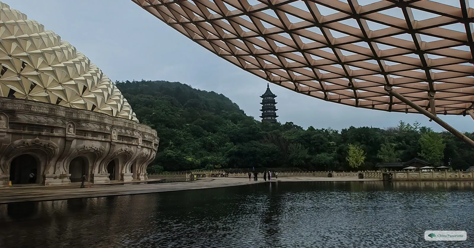 A still pool under a lattice canopy, the carved base of a dome on the left and a distant pagoda on a green hill