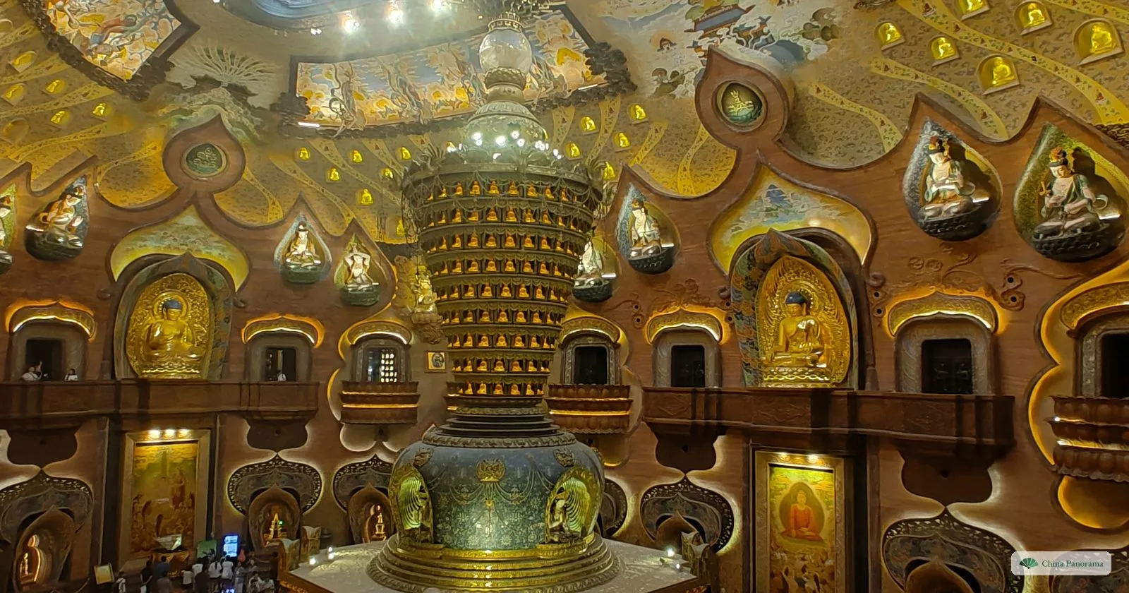 A tall stupa of blue enamel and gold standing in the middle of a round hall whose walls are lined with golden niches holding Buddha figures