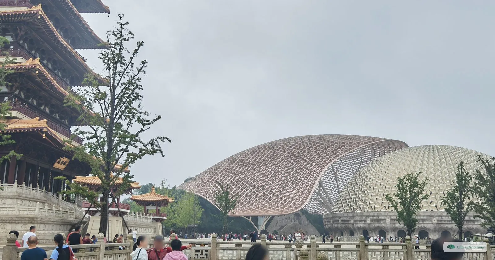 A tiered temple building with dark roofs on the left and the golden dome and lattice canopy beyond a bridge, visitors walking