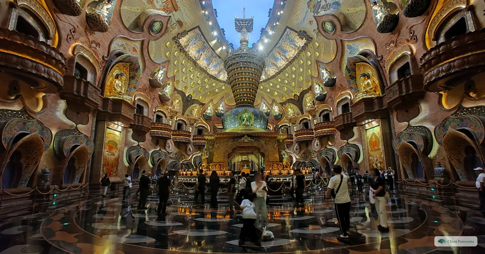 A vast domed hall of gold, bronze and carved niches with hundreds of small Buddha figures, a gilded shrine in the centre and visitors on a polished floor