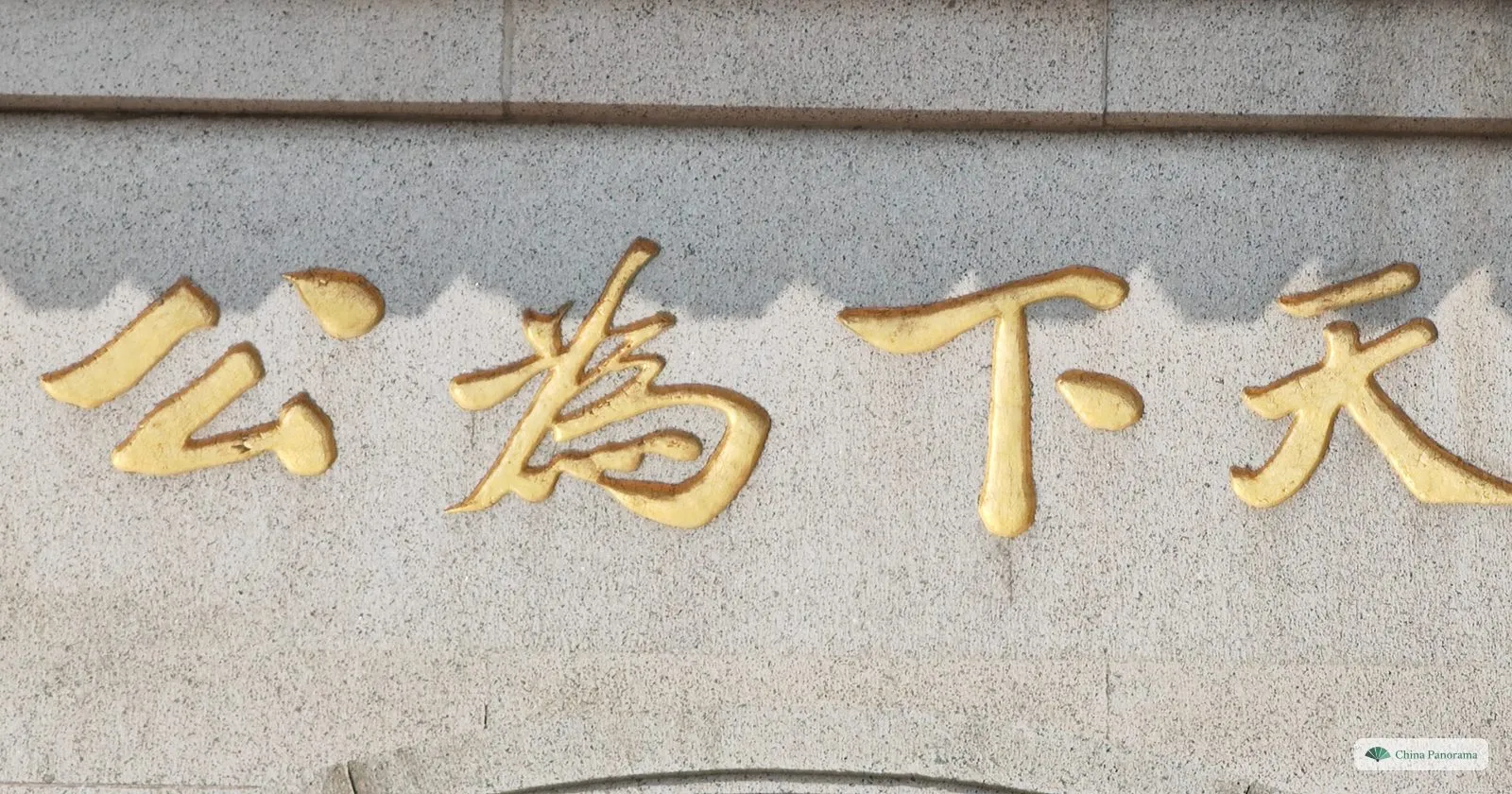 Close view of four gold characters carved into grey granite, read right to left: 天下為公