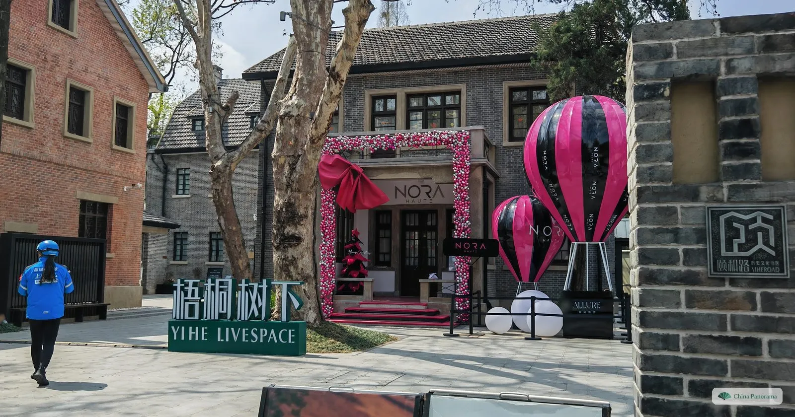 A red brick and grey brick house dressed with pink flowers and two striped balloons, a sign reading 梧桐树下 YIHE LIVESPACE in front