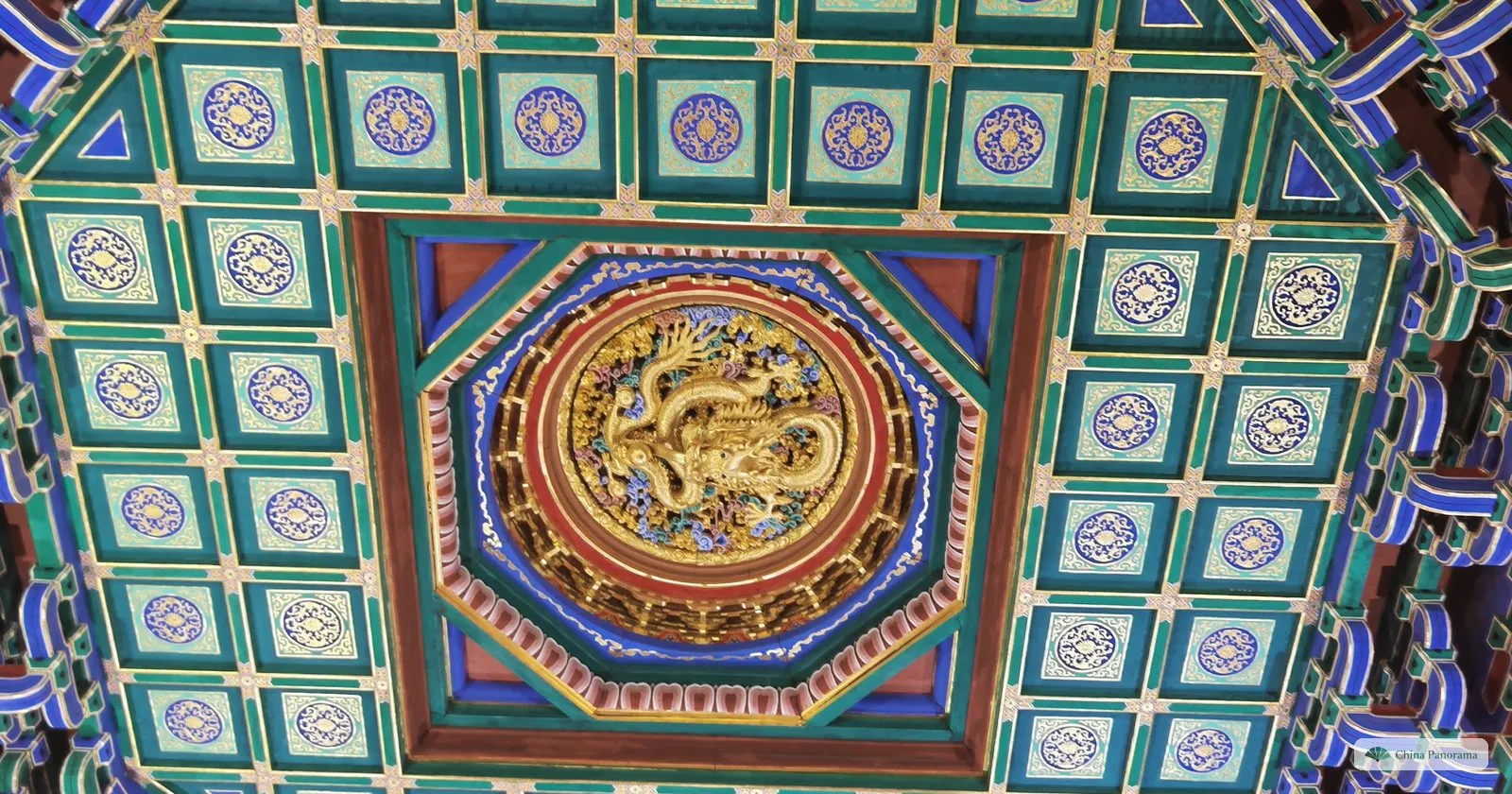 A coffered ceiling painted green, blue and gold, with a gilded carved dragon in a round panel at its centre
